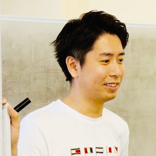 ホワイトボードの横で、マーカーを持って話している若い男性